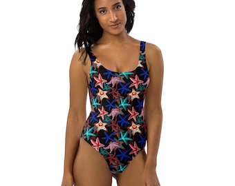 May include: A one-piece swimsuit with a black background and a pattern of colorful starfish in red, pink, blue, and teal. The swimsuit has a scoop neckline and a high-cut leg.