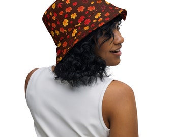 May include: A person wearing a brown bucket hat with a colorful autumn leaf pattern. The hat has a wide brim and is made of a soft, comfortable fabric.