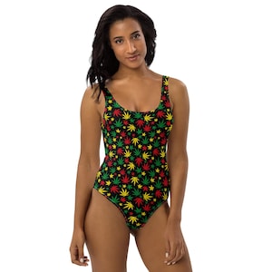 May include: A one-piece swimsuit with a black background and a pattern of red, yellow, and green cannabis leaves. The swimsuit has a scoop neckline and wide straps.