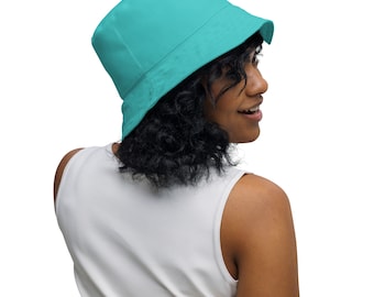 May include: A woman wearing a teal blue bucket hat and a white sleeveless shirt.