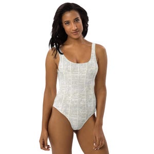 May include: One-piece swimsuit with a scoop neck and a unique all-over print. The print appears to be a collage of text, creating a vintage or literary aesthetic. The swimsuit is white with the text in a light gray color.