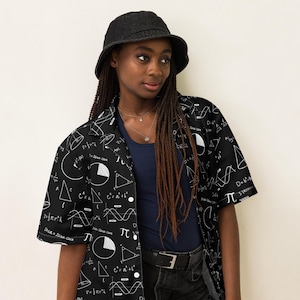 May include: A black short-sleeved button-up shirt with a white print of mathematical formulas, equations, and symbols. The shirt is worn by a person with long braids and a black bucket hat.