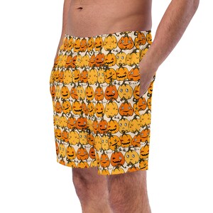 May include: A pair of cream-colored shorts with a pattern of orange and yellow jack-o'-lantern faces. The shorts have a drawstring waist and a relaxed fit.