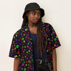 May include: A black bucket hat and a black button-down shirt with a colorful pi symbol pattern. The shirt is worn over a navy blue top and black jeans. A silver necklace is visible.
