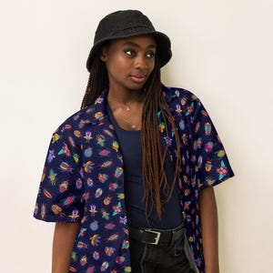 May include: A blue short-sleeved shirt with a colorful beetle pattern. The shirt has a button-up front and a collar. The model is wearing the shirt with a black bucket hat and black jeans.