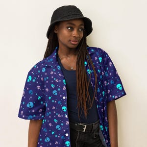 May include: A blue short-sleeved button-up shirt with a pattern of alien faces and white stars. The shirt has a collar and a button-up front.