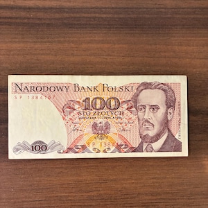 May include: A Polish 100 Zlotych banknote from 1986, featuring a portrait of Ludwik Waryński. The note has text in Polish, including "Narodowy Bank Polski" and "Sto Złotych". The serial number is SP 1384167.