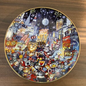 May include: A colorful ceramic plate with a New Year's Eve theme. The plate features a cityscape with fireworks, cats wearing party hats, and the text "Happy New 2000 Year".