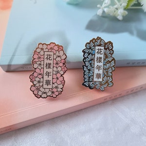 以下が含まれることがあります： 花柄と金色のアクセントが施されたエナメル製のピンが2つ。ピンには中国語で「花樣年華」という文字が書かれており、日本語に訳すと「最も美しい瞬間」という意味です。