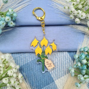 May include: A yellow flower keychain with a gold chain and a tag that says "He needs you".
