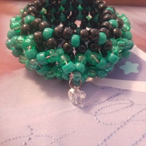 May include: A black and green beaded bracelet with a crystal charm. The bracelet is made of small, round beads and is layered in a spiral pattern.