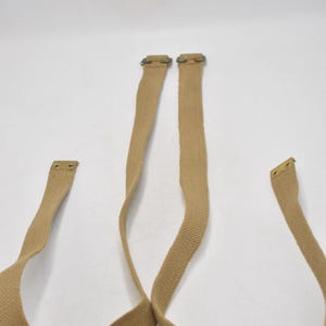 May include: Tan canvas straps with metal hardware. The straps are a light brown color and appear to be made of a durable material. The metal hardware is a brass color. The straps are likely for a bag or other item.