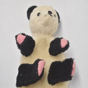 May include: A vintage stuffed animal bear with a cream-colored body, black paws and ears, and pink paw pads. The bear has a simple, classic design, with a small black nose and eyes.