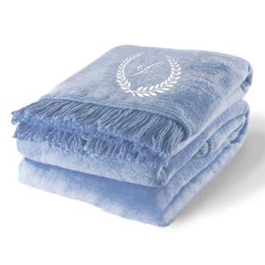 Può includere: Una morbida coperta blu con un monogramma ricamato bianco e un bordo a frangia.