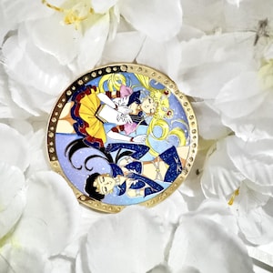 Könnte beinhalten: Ein runder Emaille-Pin mit drei Anime-Charakteren in farbenfrohen Outfits. Der Pin hat einen goldfarbenen Rand mit kleinen dekorativen Akzenten. Der Hintergrund des Pins ist ein sternenblau, und die Charaktere sind in verschiedenen Posen.