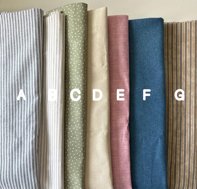 Seven neatly arranged fabric swatches labeled A to G, featuring stripes, polka dots, and solid colors in soft tones like gray, beige, olive, pink, blue, and rustic brown — fabric options for handmade textile art