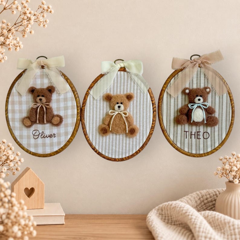 May include: Three oval embroidery hoops featuring felt teddy bears. The left hoop has a beige gingham background with the name Oliver. The center hoop has a striped background. The right hoop has a striped background with the name THEO.