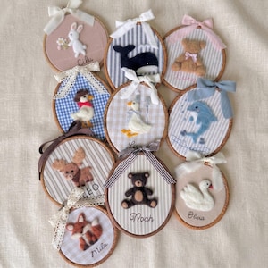 May include: A collection of nine circular embroidery hoop wall hangings featuring felt animal appliqués including a rabbit, whale, teddy bear, duck, dolphin, moose, and fox. Each hoop is decorated with a fabric background, a ribbon bow, and a name.