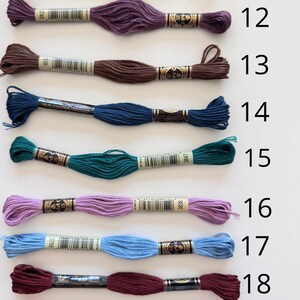 May include: Nine skeins of embroidery floss in various colors, including shades of brown, purple, teal, blue, and pink. Each skein is labeled with a number from 11 to 19. The floss is neatly arranged, showcasing the range of colors available.