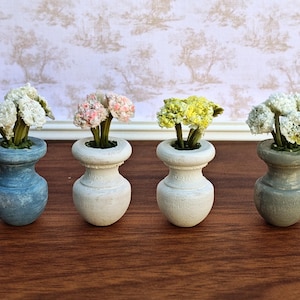 May include: Four miniature vases, each holding a small bouquet of flowers. The vases are in shades of blue, white, and gray. The flowers are white, pink, and yellow. The vases are arranged in a row on a wooden surface.