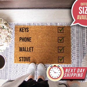 May include: A brown coir doormat with the words "KEYS", "PHONE", "WALLET", and "STOVE" printed in black. There are four checkboxes next to the words, with three of them checked in green. The doormat is on a white and gray patterned rug.