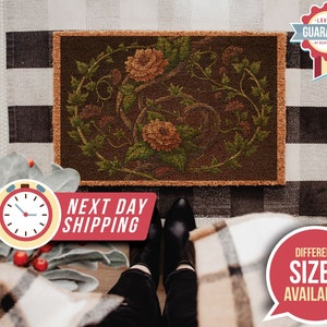 May include: A brown doormat with a floral design featuring intricate vines and orange flowers. The doormat has a textured surface and a woven border.
