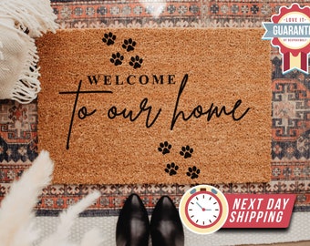 May include: Welcome to our home doormat with paw prints. The doormat is brown and has black text. The text says "Welcome to our home".