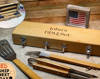 May include: A bamboo carrying case with a metal latch and handle. The case is engraved with the text "John's BBQ Set". The case contains a spatula, tongs, and a grilling fork with wooden handles.