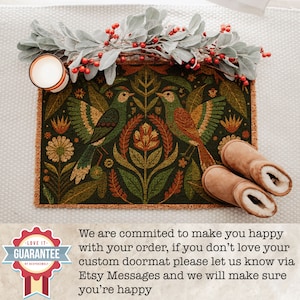 May include: A green, brown and orange doormat with a floral and bird design. The doormat has a fringed border. The text "LOVE IT - GUARANTEE" is on a red and white circular sticker.