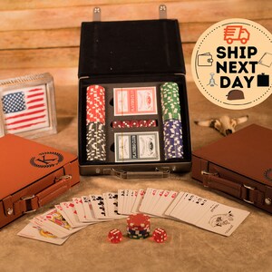 May include: A brown leatherette case with a monogrammed initial "K" and a matching case with a monogrammed initial "T". The cases contain a poker set with chips, cards, and dice. The cases are open and the contents are visible. The cases are on a wooden surface.