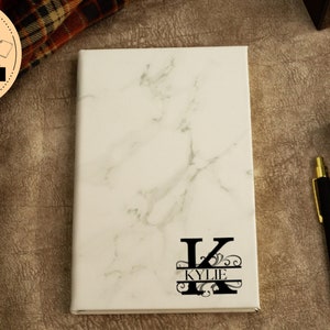 May include: White marble notebook with a black initial "K" and the name "Kylie" in a split monogram design.