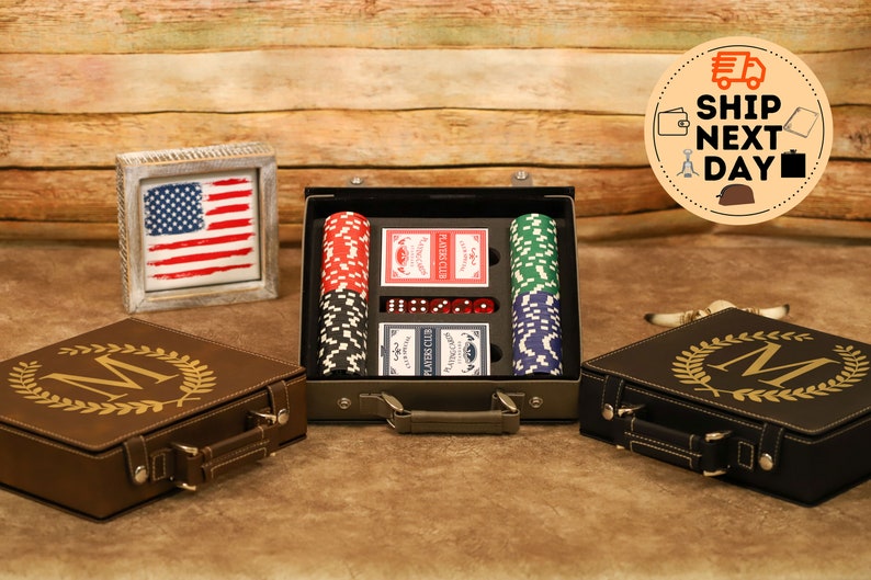 May include: A set of playing cards and poker chips in a brown leather case with a gold monogram. The case has a handle and is closed. The case is sitting on a wooden surface.