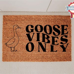 May include: A rectangular doormat with a brown coir surface. The mat features a black outline drawing of a goose on the left and the words "GOOSE VIBES ONLY" in large black letters.