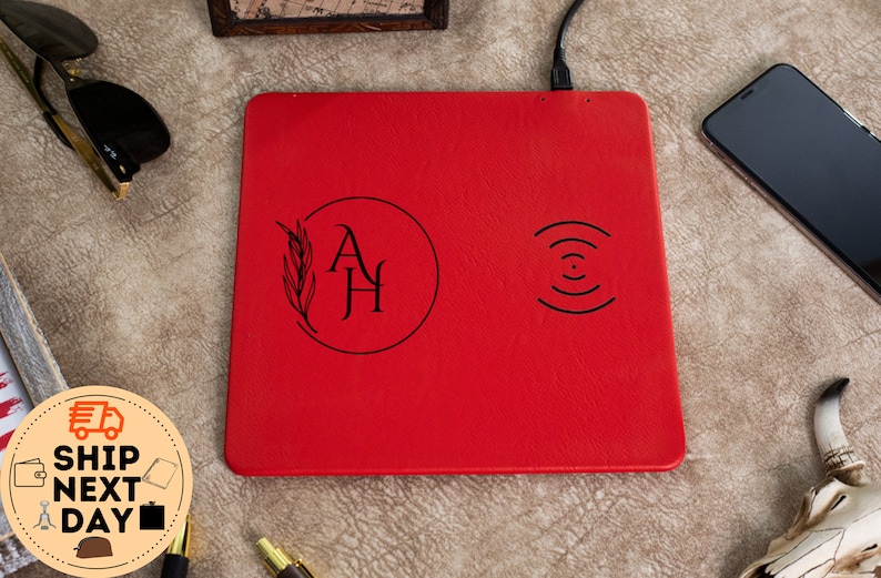 May include: Red leather wireless charging pad with a monogrammed design in a circle with a leaf design and the initials "AH". The charging pad has a wireless charging symbol on the right side.