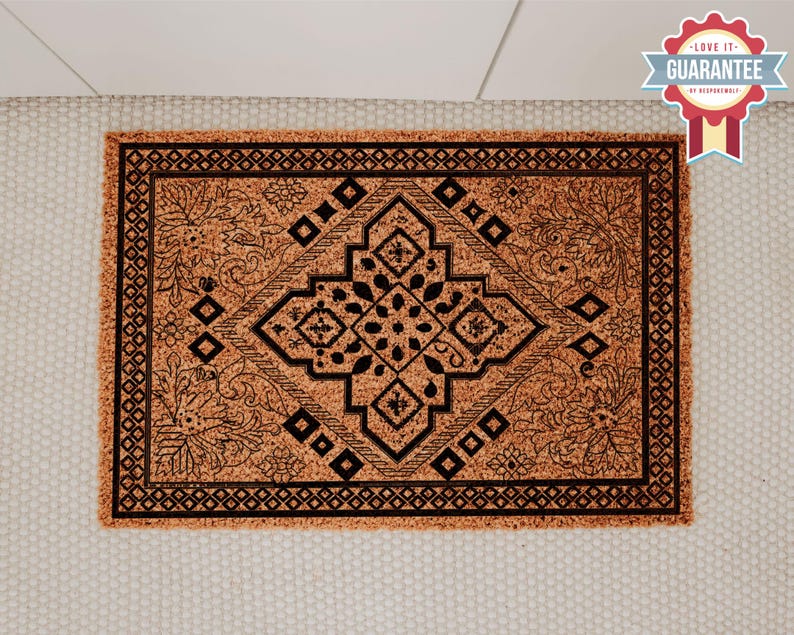 K&ouml;nnte beinhalten: Eine braune Kokosmatte mit einem schwarz-wei&szlig;en geometrischen Muster. Das Muster zeigt eine zentrale Diamantform mit komplizierten floralen Designs.