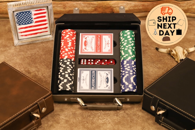 May include: A black leather carrying case with a handle, containing a set of playing cards, poker chips, and dice. The case is open, revealing the contents. The cards are labeled "Players Club" and the chips are red, green, and blue.