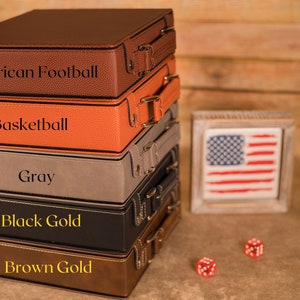 May include: A stack of five leather-bound boxes with different colored covers and engraved text. The boxes are labeled "American Football", "Basketball", "Gray", "Black Gold", and "Brown Gold".