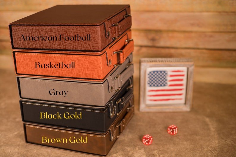 May include: A stack of five leather-bound boxes with different colored covers and engraved text. The boxes are labeled "American Football", "Basketball", "Gray", "Black Gold", and "Brown Gold".