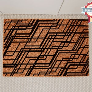 May include: A brown coir doormat with a black geometric pattern. The pattern is made up of thin lines that create a series of squares and rectangles.