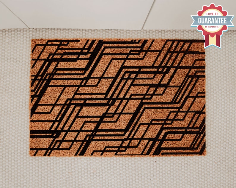 May include: A brown coir doormat with a black geometric pattern. The pattern is made up of thin lines that create a series of squares and rectangles.