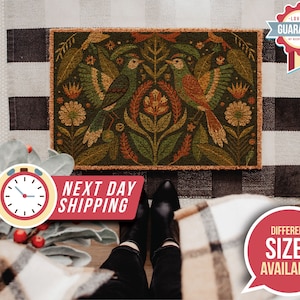 May include: A brown coir doormat with a colourful floral and bird design. The design features two birds with orange, brown, and green feathers, surrounded by green leaves and flowers with yellow, orange, and red accents.