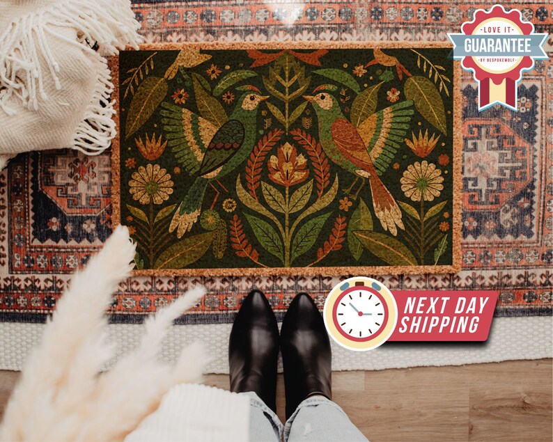 May include: A cork doormat with a green background featuring a stylised floral design with two birds in orange, yellow, and brown. The birds are facing each other and have their wings spread out. The doormat has a brown border.