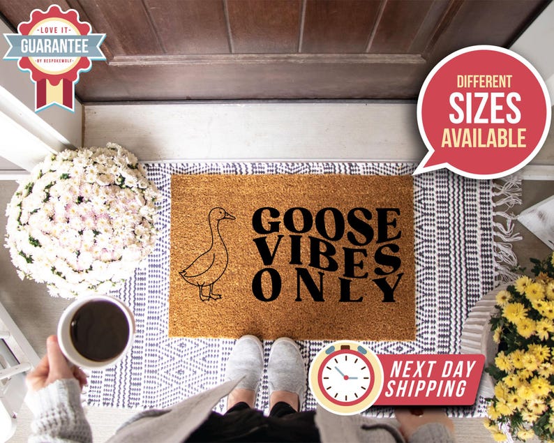 May include: A rectangular coir doormat with a goose illustration and the text "GOOSE VIBES ONLY" in black. The mat sits on a patterned rug. The image includes a person's feet, a coffee cup, and a sign indicating different sizes are available.