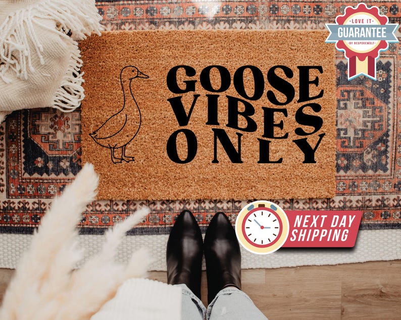 May include: A rectangular coir doormat with a goose illustration and the text "GOOSE VIBES ONLY". The mat is a natural brown colour. A guarantee badge is visible in the top right corner. The image also shows a person's feet.