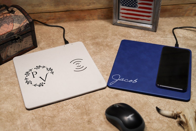 May include: Two wireless charging pads, one white with a floral monogram "PV" and a wireless charging symbol, and one blue with the name "Jacob" in white script. A black computer mouse is in the foreground.