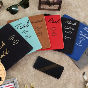 May include: A set of six wireless charging pads in various colours, including teal, brown, red, black, blue, and grey. Each pad features a stylised wireless charging symbol and text indicating the colour and material of the pad. The text includes "Teal", "Rawhide", "Red", "Black Silver", "Blue Silver", and "Grey".