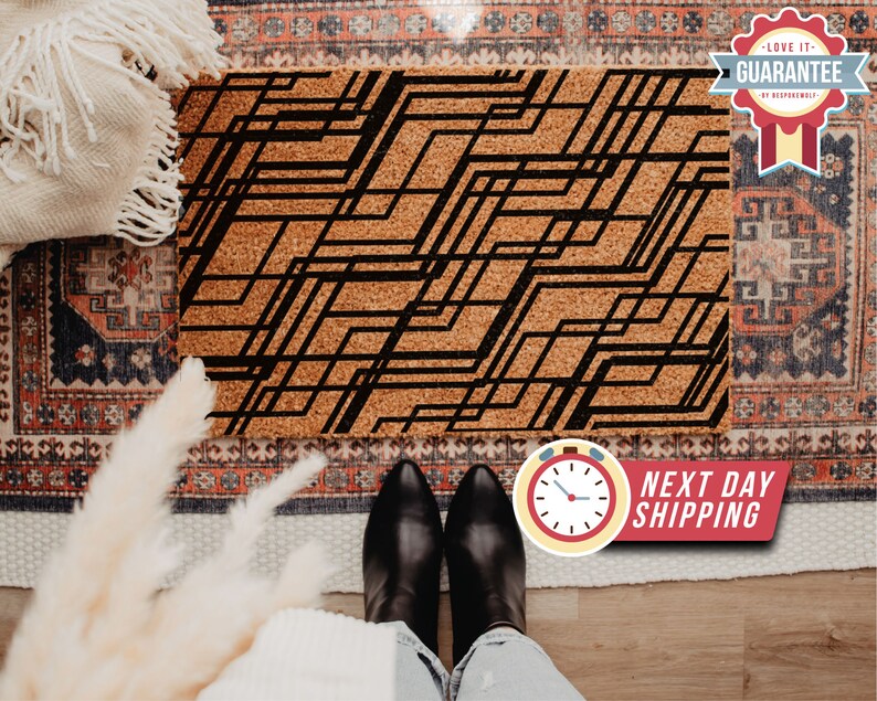 May include: A black and white geometric design printed on a cork doormat. The doormat is on a patterned rug.