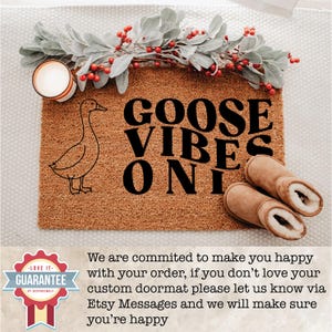 May include: A brown coir doormat with the words "GOOSE VIBES ONLY" in black. A line drawing of a goose is on the left. Two brown shearling slippers are on the right. A candle and greenery with red berries are at the top.