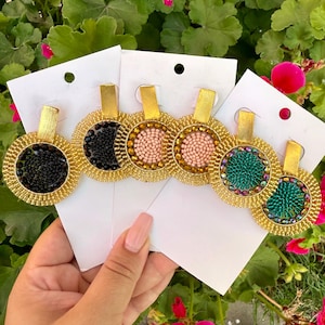 May include: Five pairs of gold-toned earrings with different coloured beaded designs. The earrings are displayed on white card stock.
