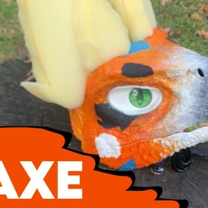 May include: A close-up of a brightly colored orange, white, and black furry animal head with green eyes. The head is on a wooden surface. The word "AXE" is written in white letters on an orange background.